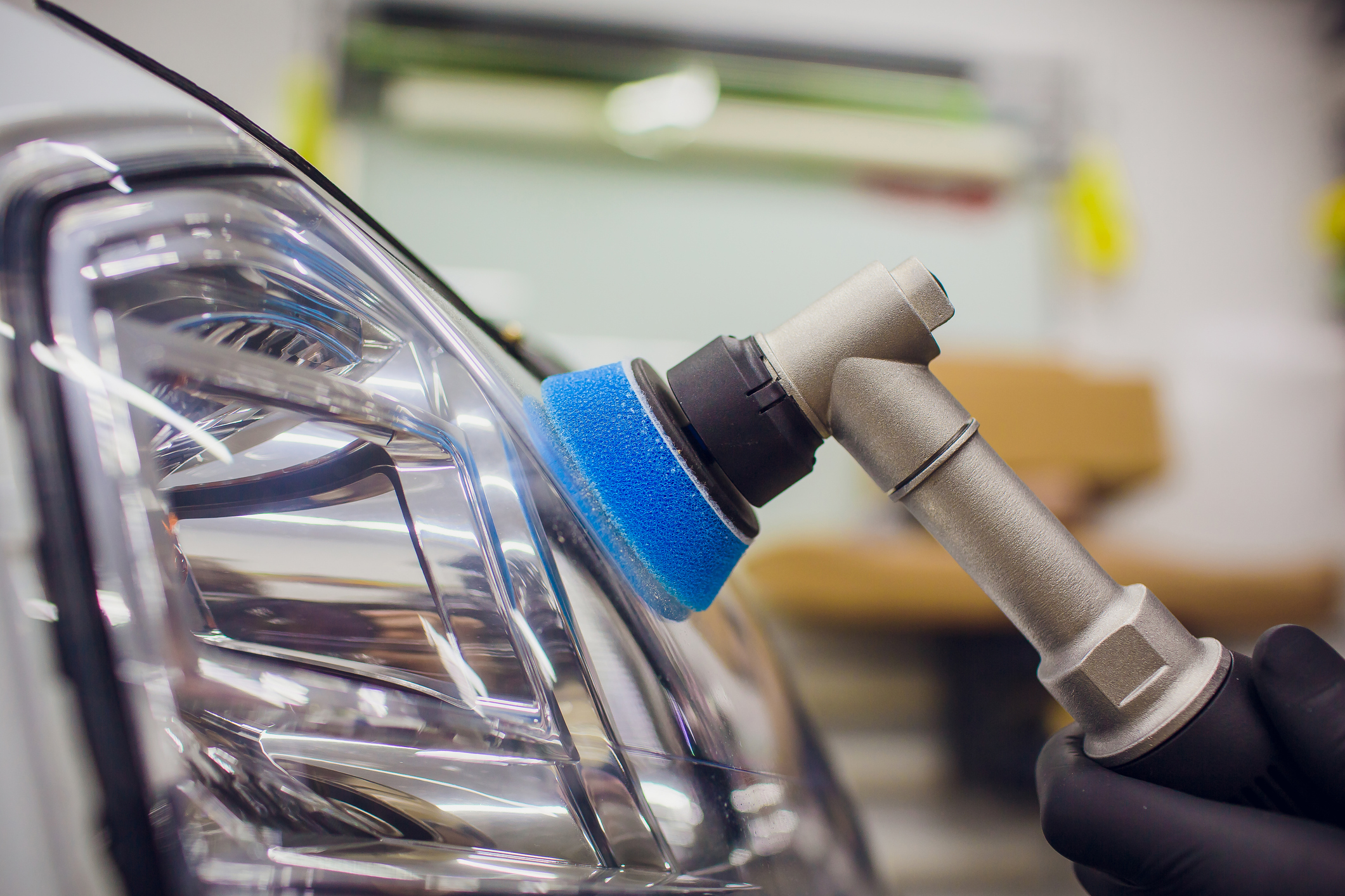 Car headlight being polished with tool.