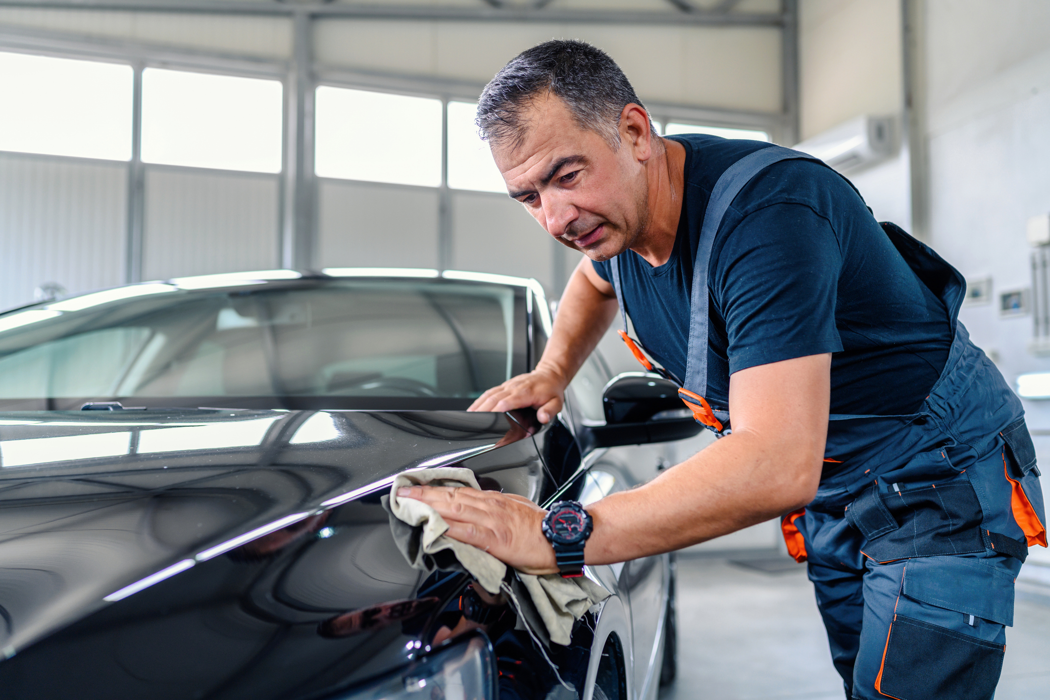 Man polishing a black car in garage.